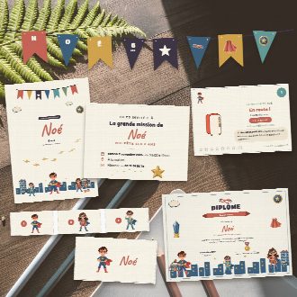Le kit L'École des Super-Héros complet étalé sur une table : invitations, affiche, chasse au trésor, marque-places, diplôme et guirlande au prénom de l’enfant