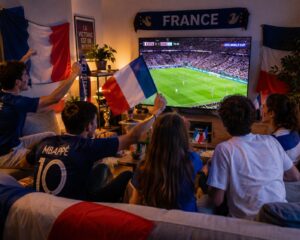 Amis réunis dans un salon avec drapeaux tricolores devant un match de la Coupe du Monde 2026 à la télé