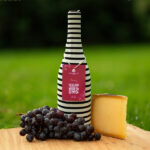 Bouteille de vin masquée d'une housse rayée pour dégustation à l'aveugle, entre raisin noir et fromage