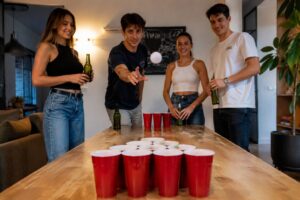 Quatre amis autour d'une table de beer pong, une balle en vol vers les gobelets rouges pendant une soirée jeux TikTok