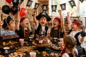 Anniversaire pirate : cinq enfants déguisés acclament le gâteau au chocolat sous une guirlande tête de mort