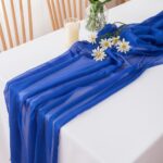 Chemin de table en voile bleu roi sur nappe blanche, ponctué de marguerites blanches