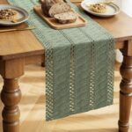 Chemin de table vert sauge en dentelle ajourée déroulé sur une table en bois avec pain et tartelettes