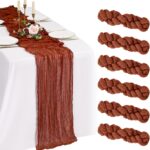 Chemin de table en gaze terracotta sur nappe blanche, accompagné de roses et de bougies dorées