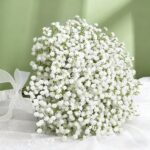 Bouquet rond de gypsophile blanche noué d'un ruban sur une nappe brodée, fond vert sauge
