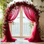 Arche de mariage drapée de voilage framboise et fleurie de roses rouges face à la mer