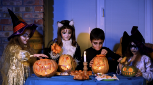 Enfants déguisés en sorcière et chat noir autour de citrouilles sculptées pour des jeux d'Halloween à la maison