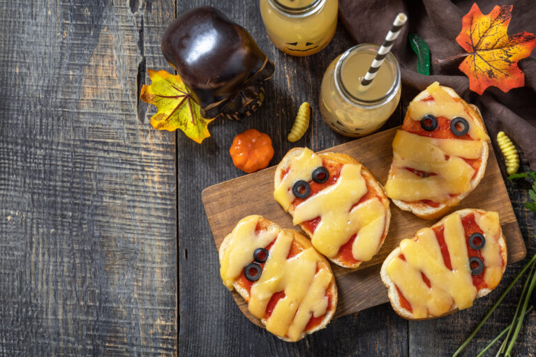 Mini-pizzas momies aux bandes de fromage et yeux d'olives sur planche en bois, recette du goûter d'Halloween