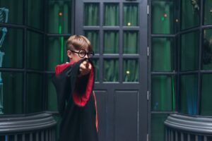Garçon à lunettes rondes en robe de sorcier qui pointe sa baguette dans un décor vert d'anniversaire Harry Potter