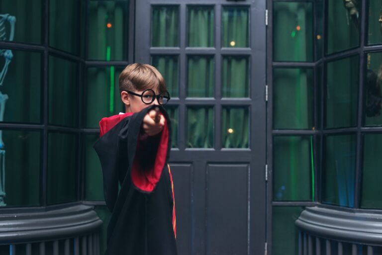 Garçon à lunettes rondes en robe de sorcier qui pointe sa baguette dans un décor vert d'anniversaire Harry Potter