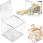 Boîtes cubiques transparentes en plexiglas remplies de dragées pastel, dont une nouée d'un ruban pêche