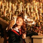 Bougies flottantes lumineuses au-dessus d'une fillette déguisée en élève de Gryffondor tenant une chouette et une baguette