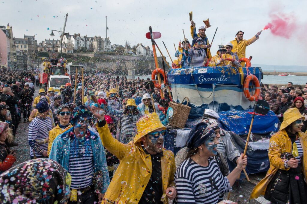 Carnavaliers en cirés jaunes et marinières autour d'un char en forme de bateau au carnaval de Granville