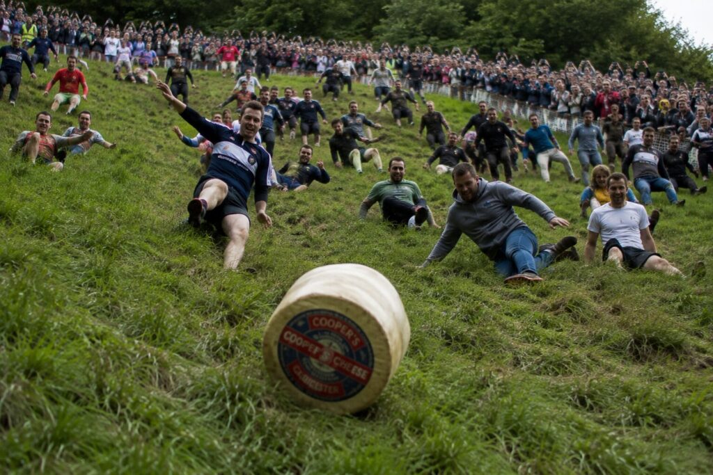 Concurrents dévalant une pente herbeuse derrière une meule de fromage lors du Cheese Rolling de Cooper's Hill