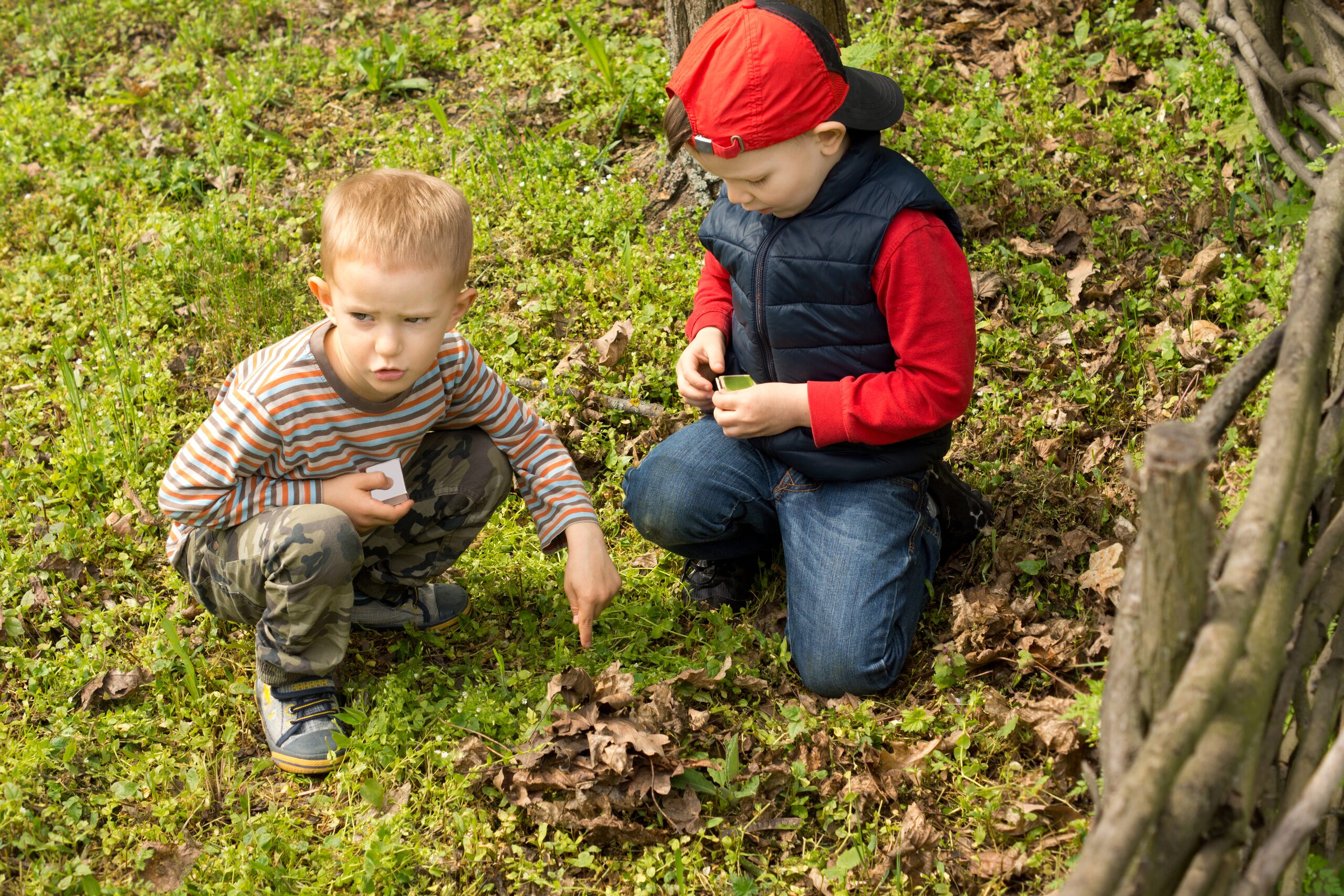 Chasse au trésor à 5 ans dans le jardin : deux enfants accroupis cherchent la cachette suivante, carte en main