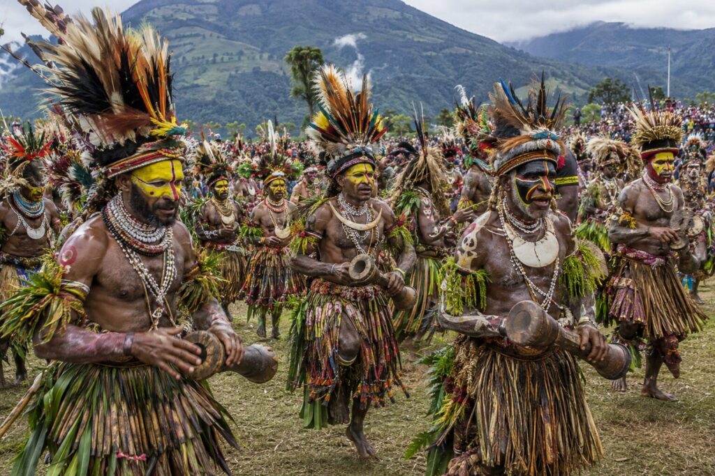Danseurs aux visages peints en jaune, coiffes de plumes et pagnes végétaux au Goroka Show en Papouasie
