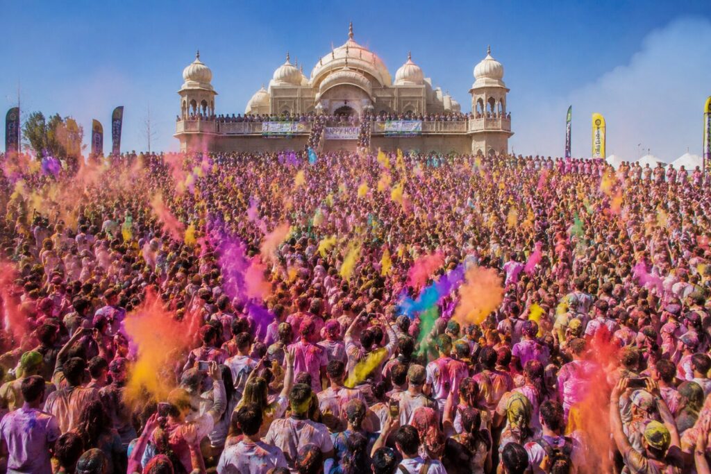 Foule couverte de poudres colorées roses, jaunes et violettes devant un temple blanc pendant la fête de Holi en Inde