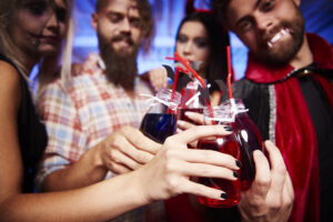 Amis déguisés en vampire et en sorcière trinquant avec des cocktails rouges lors d'une murder party d'Halloween