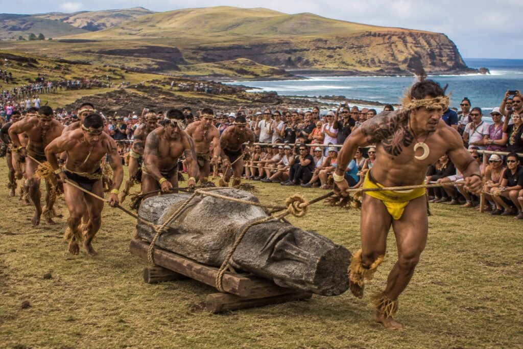 Hommes au corps peint tirant une statue moaï couchée devant la foule pendant le Tapati Rapa Nui sur l'île de Pâques