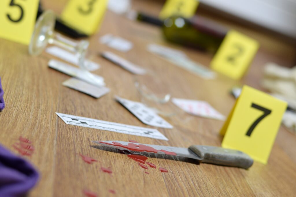 Scène de crime reconstituée avec marqueurs de preuves jaunes numérotés, couteau et taches rouges pour une murder party